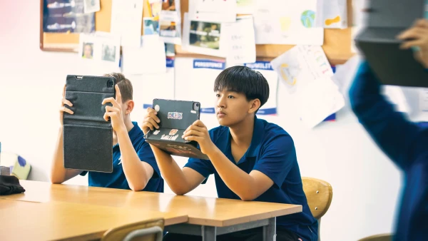 male students at international school of qingdao using a tablet to take notes in class