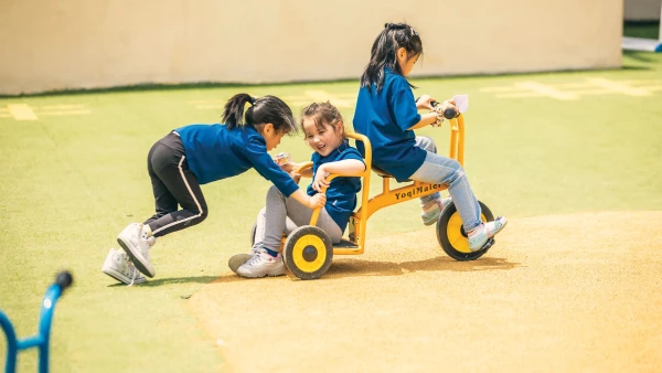 three young female students riding a tricycle at international school of qingdao early childhood learning